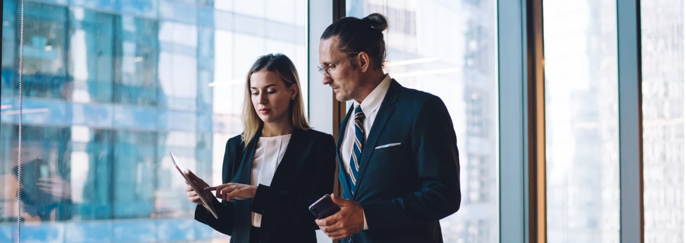 2 people standing by a window with an office background