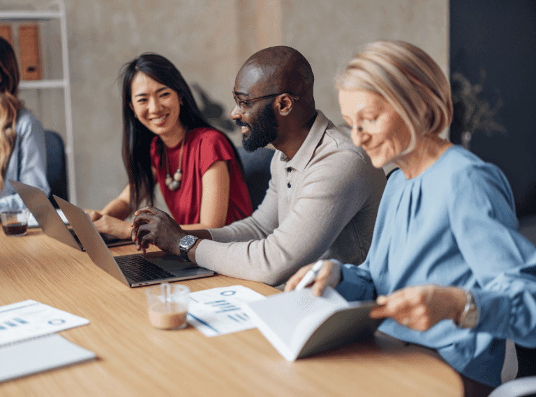 Diverse business team collaborating at a conference table with laptops and documents in a modern office setting.