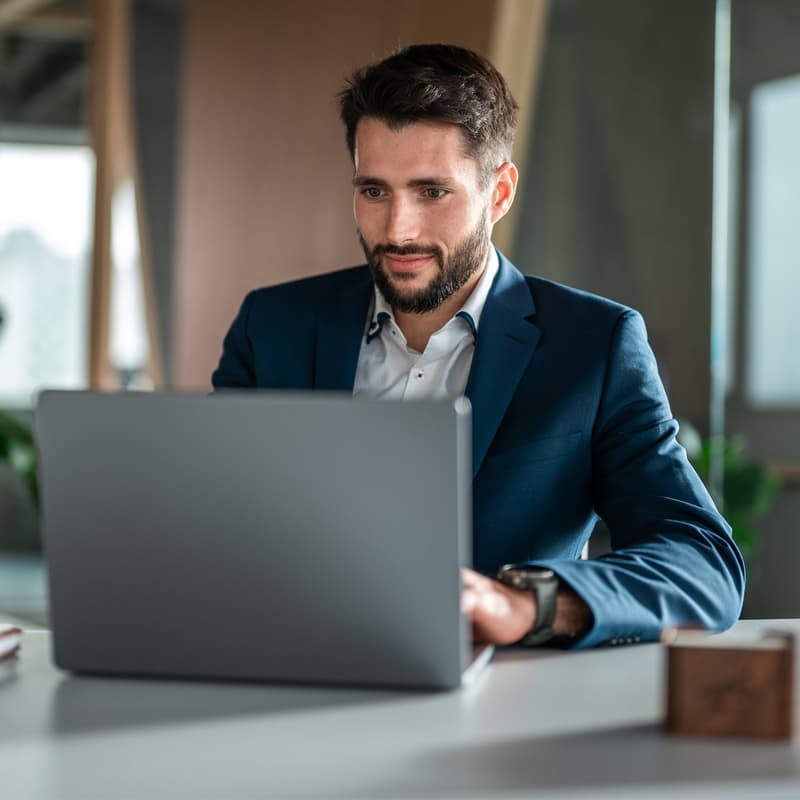 A Caucasian male businessman engages with a laptop while dressed in formal attire, conveying productivity within an office setting.