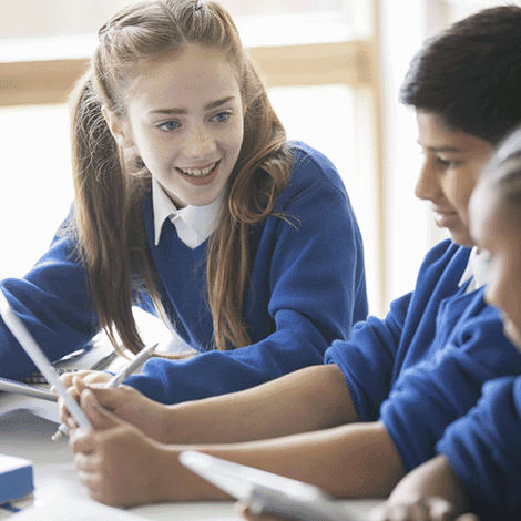 Primary school girl with strawberry blonde hair sitting next to two friends, talking excitedly.