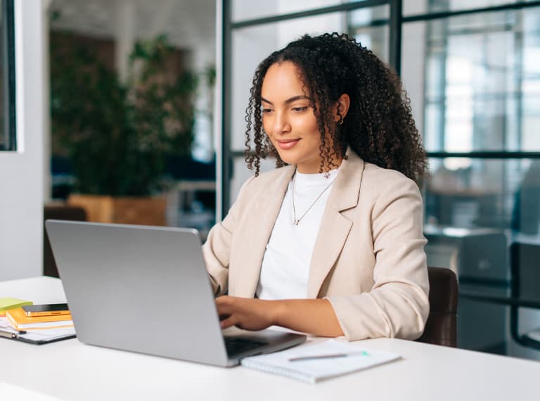 Woman uses laptop. Successful curly haired Hispanic or Brazilian woman in stylish elegant clothes, office employee, secretary or hr manager, using a laptop while sitting at her workplace, working.
