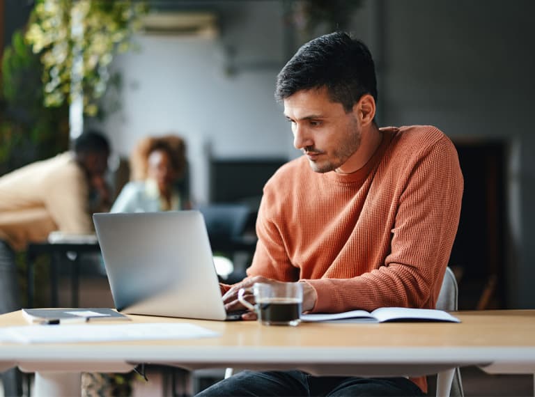 A serious Caucasian entrepreneur typing on his laptop while sitting at the office desk.