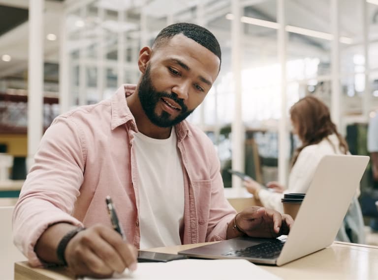 Writing, creative and man with laptop in office for business, project or research in startup. Computer, notes and African professional copywriter working on book for planning, web schedule and email.