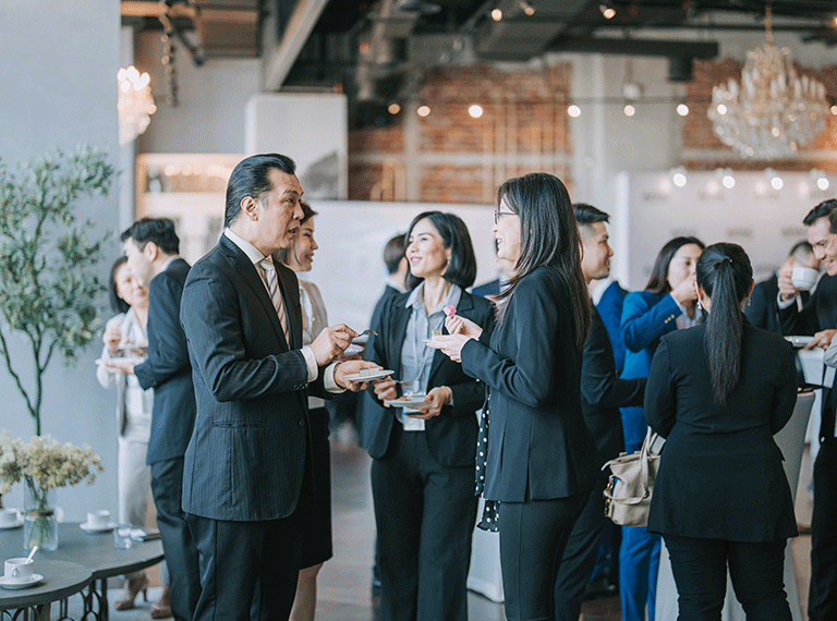 Business professionals networking at an indoor event, holding plates and drinks while conversing in a modern venue.