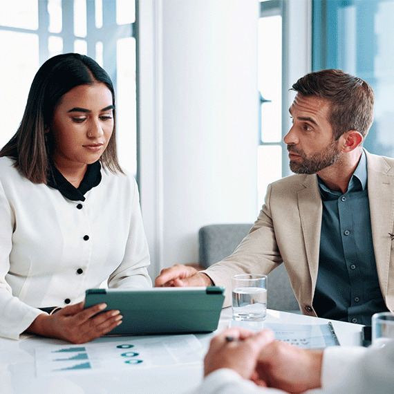 Business professionals in meeting reviewing documents on tablet with charts and graphs on table in bright office.