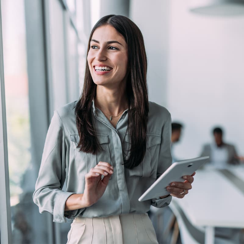 Shot of a smiling businesswoman standing in front of her team and using digital tablet. Portrait of successful businesswoman standing with her colleagues working in background.